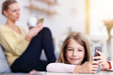 Genç anne ve küçük kızı evde kanepede oturan ve smartphone kullanarak