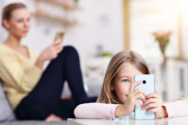 Ung mamma och hennes lilla dotter med smartphone och sitter på soffan hemma — Stockfoto