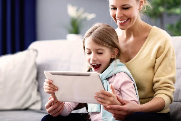 Dziewczynka i jej Mama, siedząc na kanapie w domu za pomocą tabletu — Zdjęcie stockowe