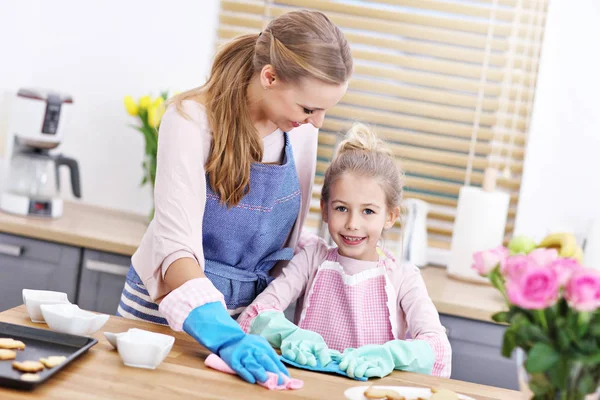 Klein meisje en haar moeder in schorten schoonmaken van de keuken — Stockfoto