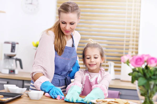 Klein meisje en haar moeder in schorten schoonmaken van de keuken — Stockfoto