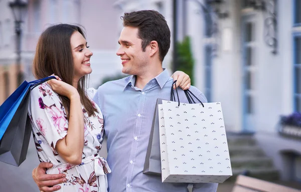 Retrato de pareja feliz con bolsas de compras en la ciudad sonriendo y abrazando . — Foto de Stock