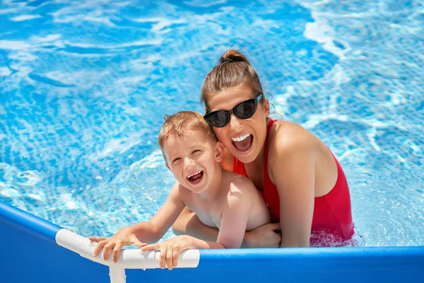 Rapaz bonito com sua mãe brincando na piscina durante o verão — Fotografia de Stock
