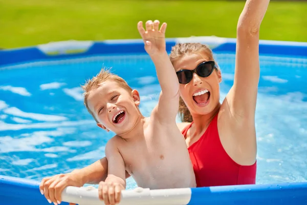 Lindo chico con su madre jugando en la piscina durante el verano — Foto de Stock