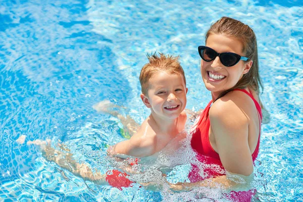 Cute boy with his mother playing in swimming pool during summer — Stock Photo, Image