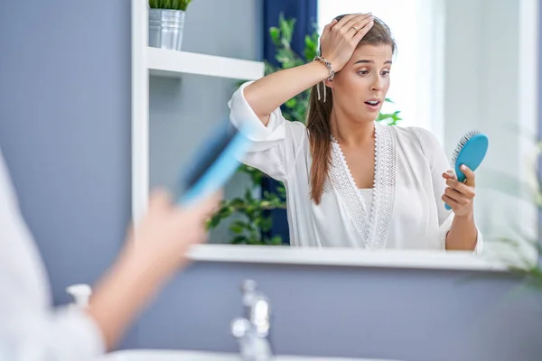 Gelukkige vrouw borstelen haar in de badkamer met probleem met haaruitval — Stockfoto