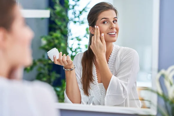 Красива брюнетка жінка застосовує крем для обличчя у ванній — стокове фото