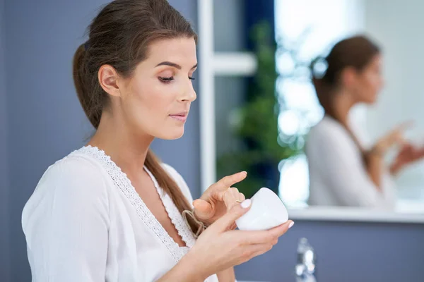 Mulher morena bonita aplicando creme facial no banheiro — Fotografia de Stock