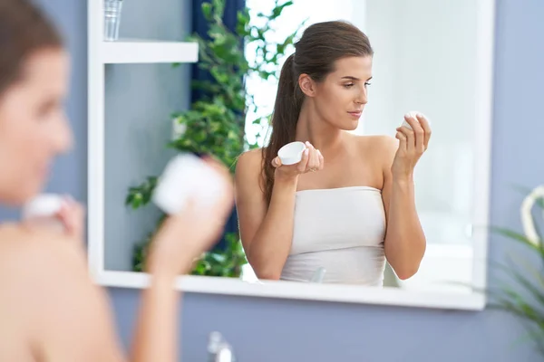 Mooie brunette vrouw die gezichtscrème aanbrengt in de badkamer — Stockfoto