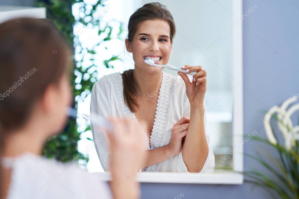 Beautiful brunette woman brushing teeth in the bathroom