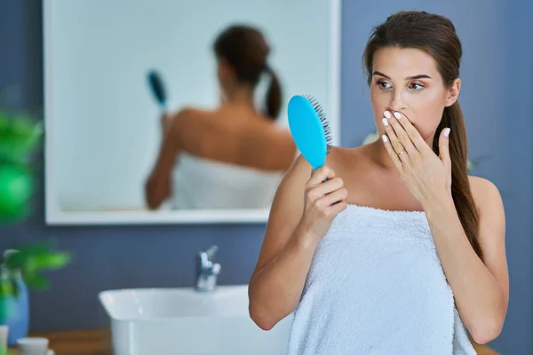 Mujer feliz cepillando el cabello en el baño teniendo problemas con la pérdida de cabello —  Fotos de Stock