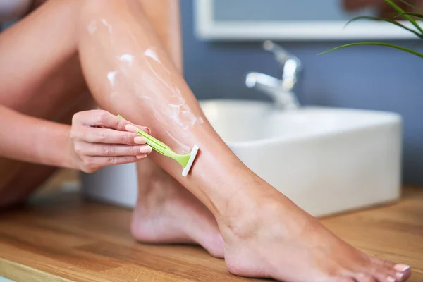 Красивая женщина бреет ноги в ванной комнате — стоковое фото