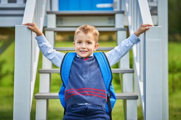 Menino pré-escolar feliz pequeno com mochila posando ao ar livre — Fotografia de Stock