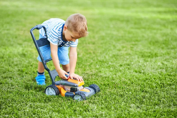 Szczęśliwy 3 rok stary chłopak mający zabawa koszenie trawnik — Zdjęcie stockowe