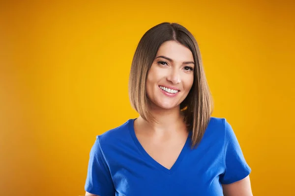 Close-up van de vrouw in blauw t-shirt kijken naar camera over gele achtergrond — Stockfoto