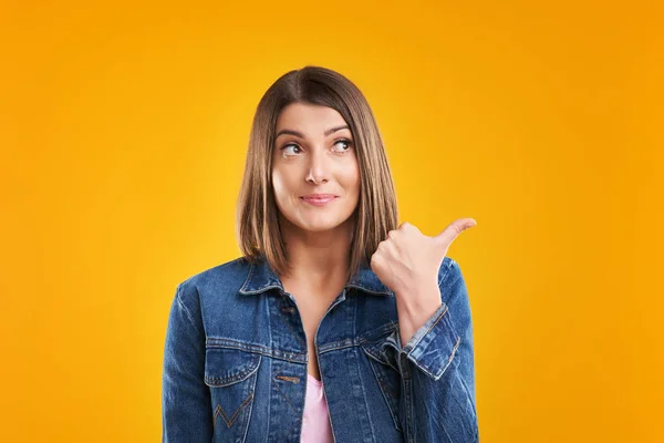 Primer plano de la mujer en chaqueta de mezclilla pensando y señalando sobre el fondo amarillo —  Fotos de Stock