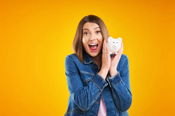 Close up of woman in denim jacket holding piggy bank over yellow background — Stock Photo, Image