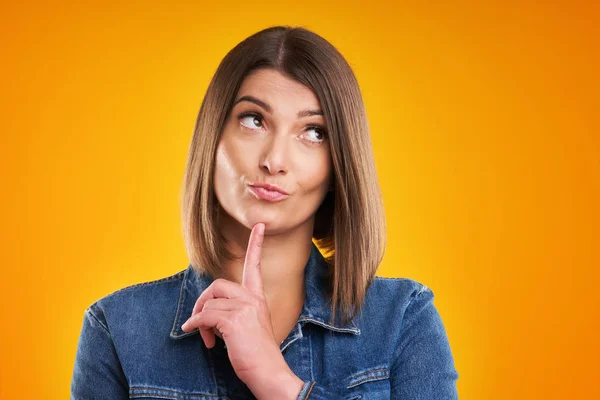 Primer plano de la mujer en chaqueta de mezclilla pensando y señalando sobre el fondo amarillo —  Fotos de Stock