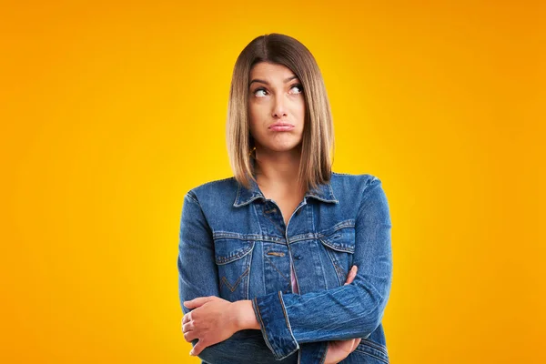 Primer plano de la mujer en chaqueta de mezclilla pensando y señalando sobre el fondo amarillo —  Fotos de Stock