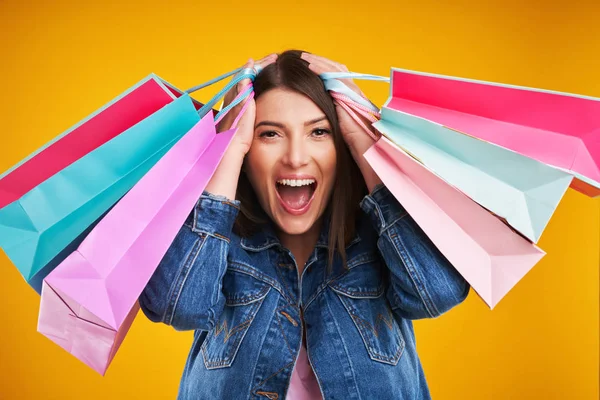 Close up of woman in denim jacket with shopping bags over yellow background — Stock Photo, Image