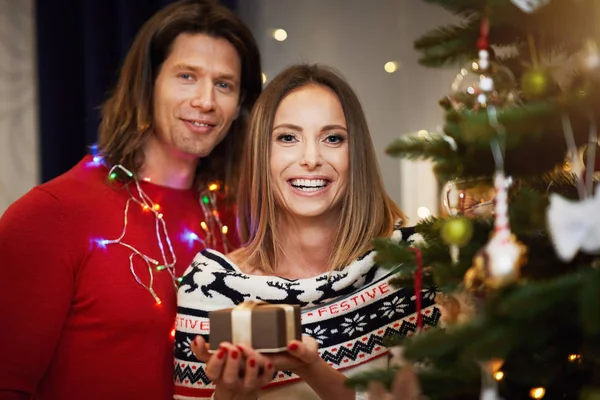 Beautiful adult couple with present over Christmas tree — Stock Photo, Image