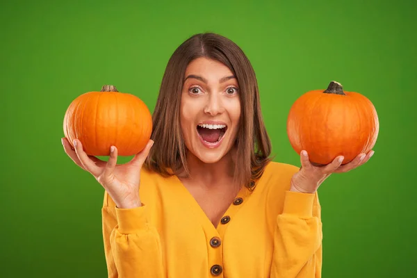 Close up of woman in yellow sweater holding pumpkin over green background — Stock Photo, Image