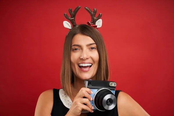 Noel ruh hali içinde Yetişkin mutlu kadın kırmızı arka plan üzerinde anlık fotoğraf çekmek — Stok fotoğraf