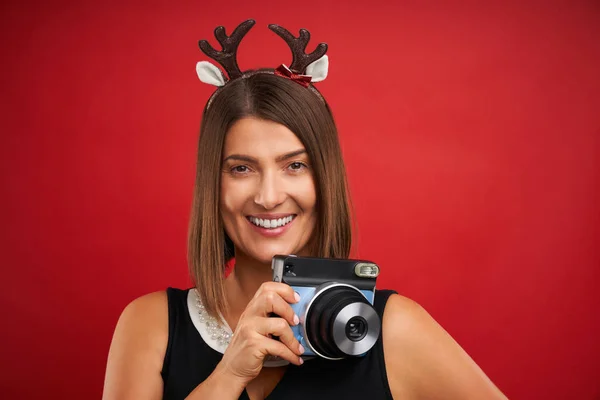 赤い背景の上にインスタント写真を撮るクリスマス気分の大人の幸せな女性 — ストック写真