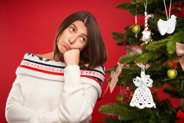 Müde Frau schmückt Weihnachtsbaum auf rotem Hintergrund — Stockfoto