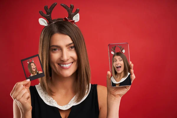 Woman in Christmas mood comparing instant pictures to smartphone camera over red — Stock Photo, Image