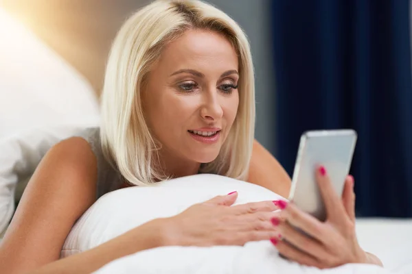 Volwassen mooie vrouw wakker volledig uitgerust en met behulp van smartphone — Stockfoto