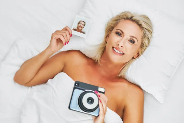 Dospělá krásná žena pořizující okamžitou fotografii v posteli — Stock fotografie