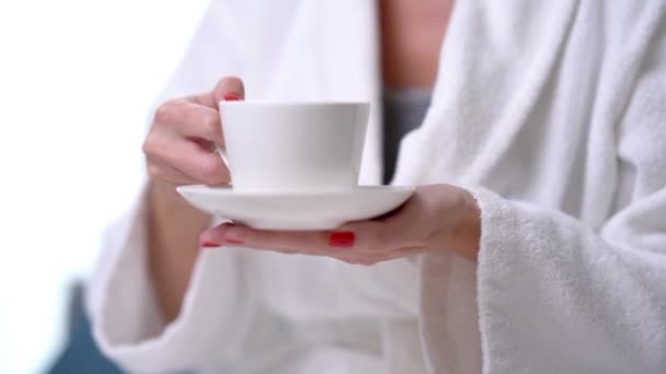 Ενήλικες ξανθιά γυναίκα πίνοντας καφέ στο μπουρνούζι το πρωί, εστίαση στο κύπελλο. — Αρχείο Βίντεο