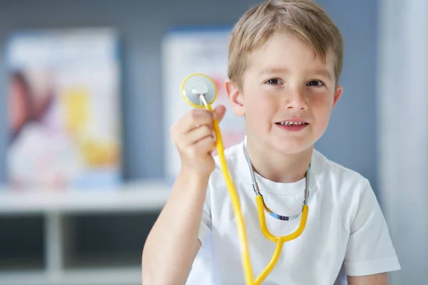 Malý doktor se stetoskopem, který se usmívá v ordinaci. — Stock fotografie