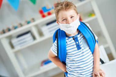 Koronavirüs salgınından dolayı maske takmış anaokulundaki sevimli küçük çocuk.