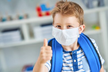 Koronavirüs salgınından dolayı maske takmış anaokulundaki sevimli küçük çocuk.