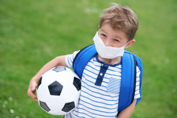 Förtjusande liten pojke med fotboll och skyddande mask på planen — Stockfoto