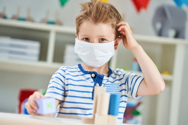 Förtjusande liten pojke på dagis med mask på grund av coronavirus pandemi — Stockfoto