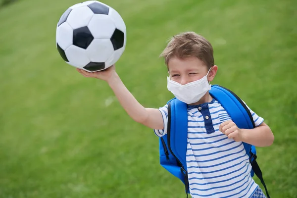 Adorable niño pequeño con el fútbol y máscara protectora en el campo —  Fotos de Stock