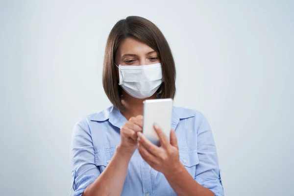 Attractive woman wearing protective mask holding smartphone isolated over white background — Stock Photo, Image