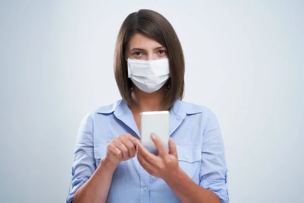 Donna attraente che indossa maschera protettiva tenendo smartphone isolato su sfondo bianco — Foto Stock