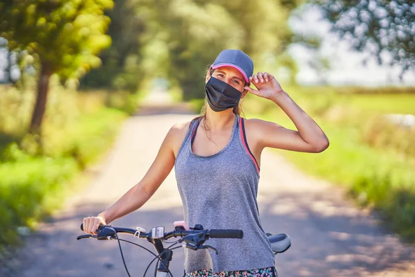Mujer joven en una bicicleta en el campo con una máscara —  Fotos de Stock