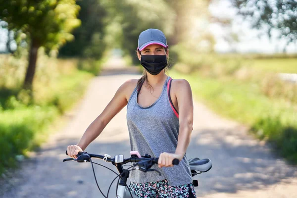 Mujer joven en una bicicleta en el campo con una máscara —  Fotos de Stock