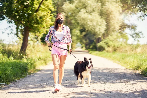 Bild einer erwachsenen Frau, die mit ihrem Haustier spazieren geht und eine Maske trägt — Stockfoto