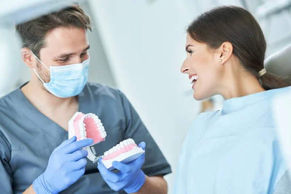 Dentista masculino mostrando mandíbula para mulher no consultório odontológico — Fotografia de Stock