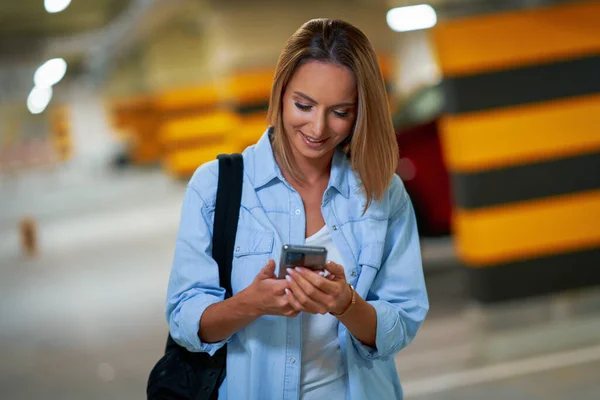 Volwassen vrouw met behulp van mobiele telefoon op de ondergrondse parkeerplaats — Stockfoto