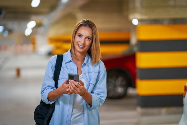 Dospělá žena používající mobil na podzemním parkovišti — Stock fotografie