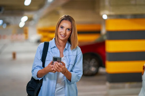 Dorosła kobieta korzystająca z telefonu komórkowego na podziemnym parkingu — Zdjęcie stockowe