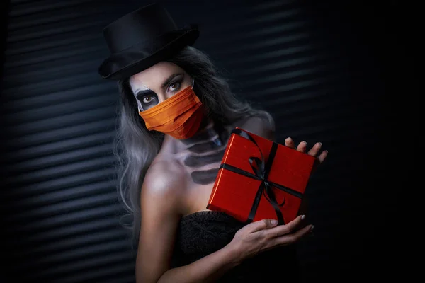 Spooky portrait of woman in gotic makeup wearing mask and holding present — Stock Photo, Image