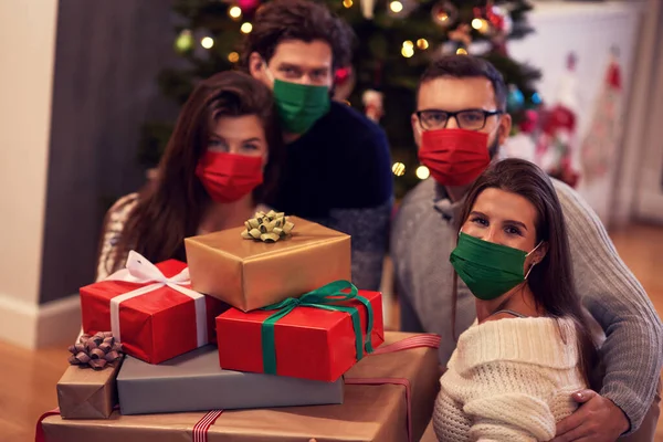 Grupo de amigos con máscaras que intercambian regalos de Navidad en casa —  Fotos de Stock